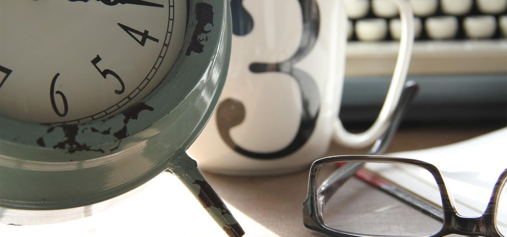 Mesa de trabajo con un despertador, una taza y unas gafas